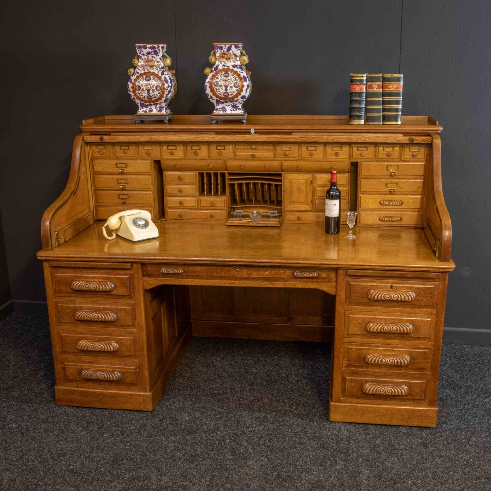 A large Edwardian golden oak roll-top desk featuring a slatted tambour cover, an extensive fitted interior with small drawers and pigeonholes, and twin pedestals with carved wooden handles. View XII