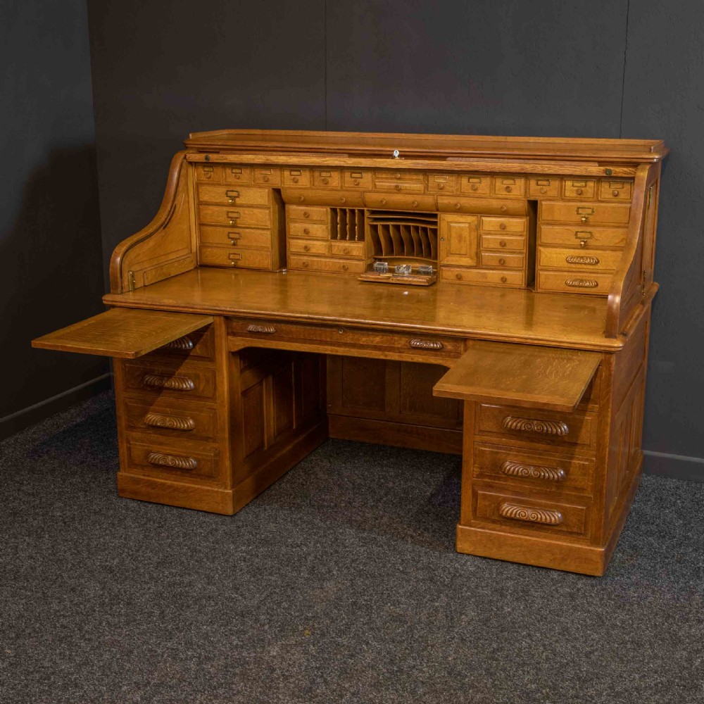 A large Edwardian golden oak roll-top desk featuring a slatted tambour cover, an extensive fitted interior with small drawers and pigeonholes, and twin pedestals with carved wooden handles. View XIII