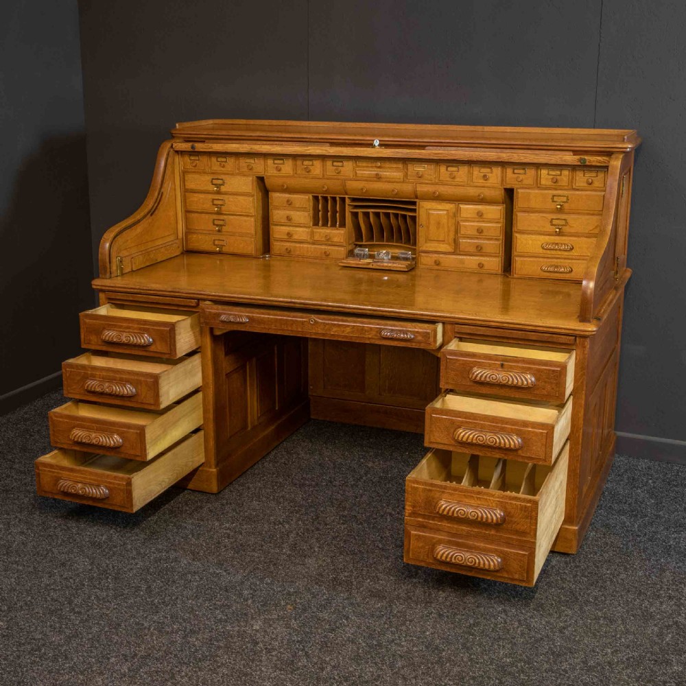 A large Edwardian golden oak roll-top desk featuring a slatted tambour cover, an extensive fitted interior with small drawers and pigeonholes, and twin pedestals with carved wooden handles. View XIV