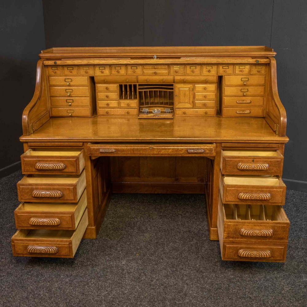 A large Edwardian golden oak roll-top desk featuring a slatted tambour cover, an extensive fitted interior with small drawers and pigeonholes, and twin pedestals with carved wooden handles. View XV