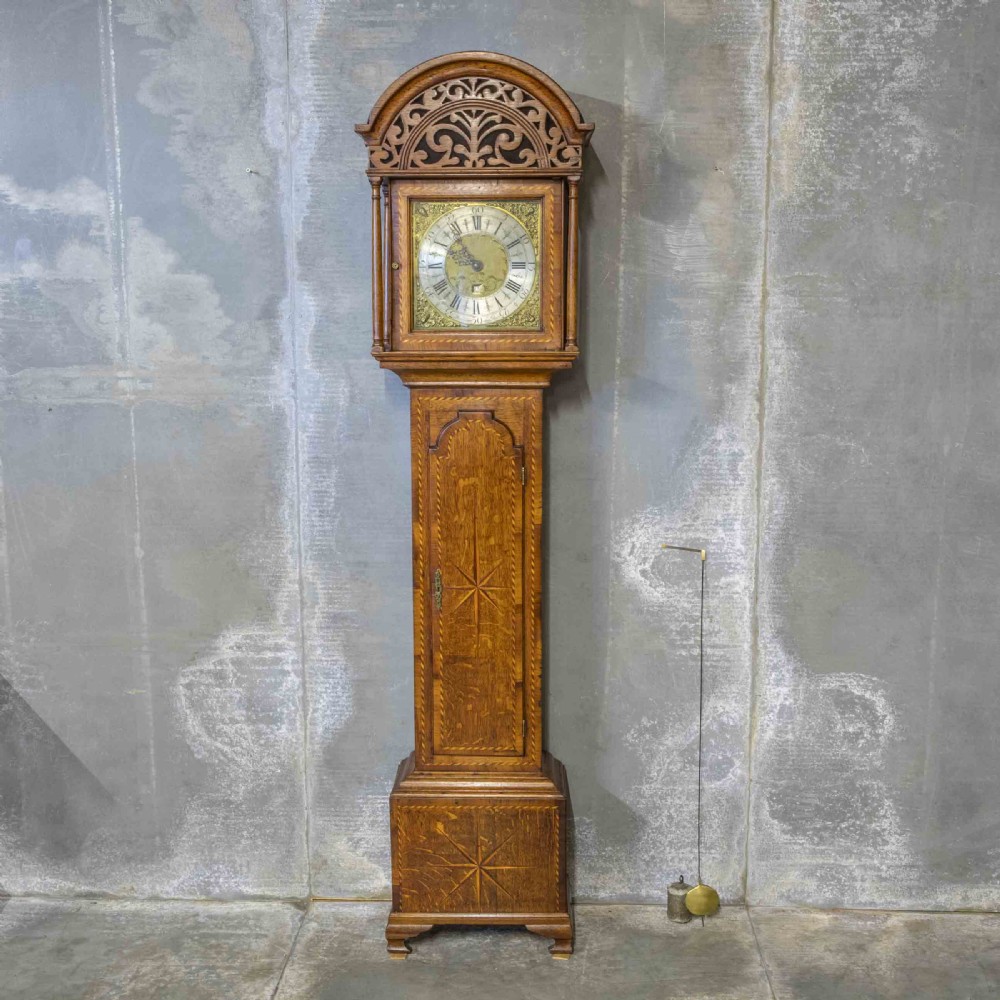 A tall Georgian carved oak longcase clock featuring an arched fretwork pediment, a brass square dial with Roman numerals, star inlay detailing on the trunk door, and a plinth base.