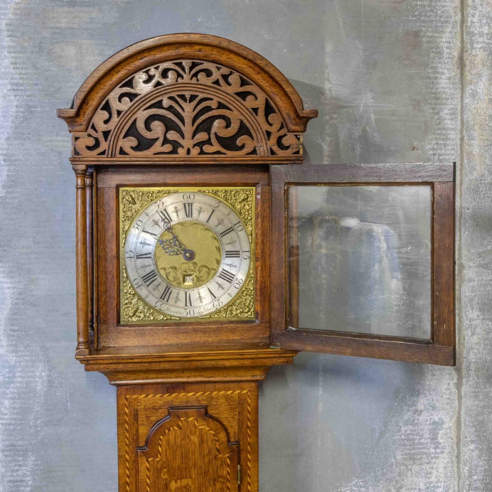 A tall Georgian carved oak longcase clock featuring an arched fretwork pediment, a brass square dial with Roman numerals, star inlay detailing on the trunk door, and a plinth base. View III