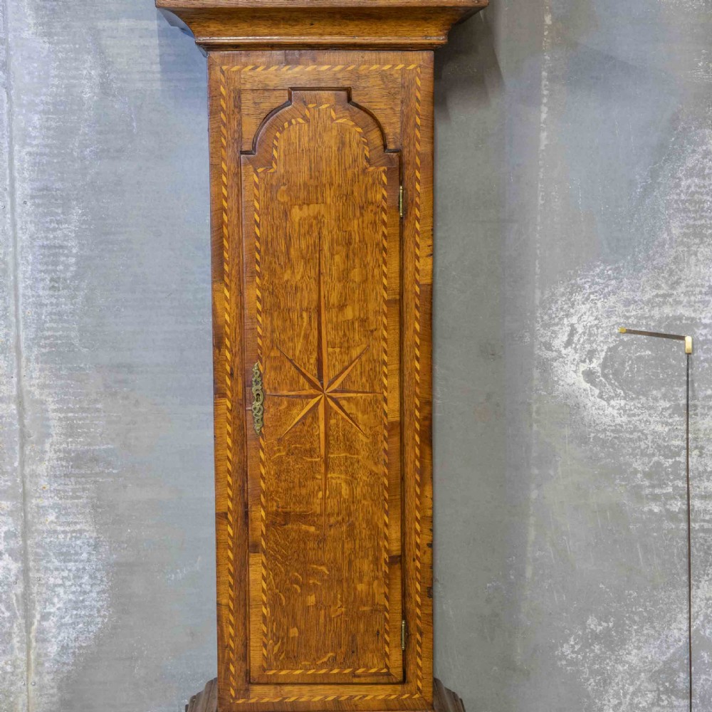 A tall Georgian carved oak longcase clock featuring an arched fretwork pediment, a brass square dial with Roman numerals, star inlay detailing on the trunk door, and a plinth base. View V