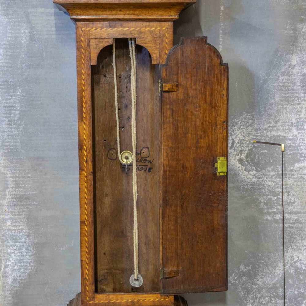 A tall Georgian carved oak longcase clock featuring an arched fretwork pediment, a brass square dial with Roman numerals, star inlay detailing on the trunk door, and a plinth base. View VI