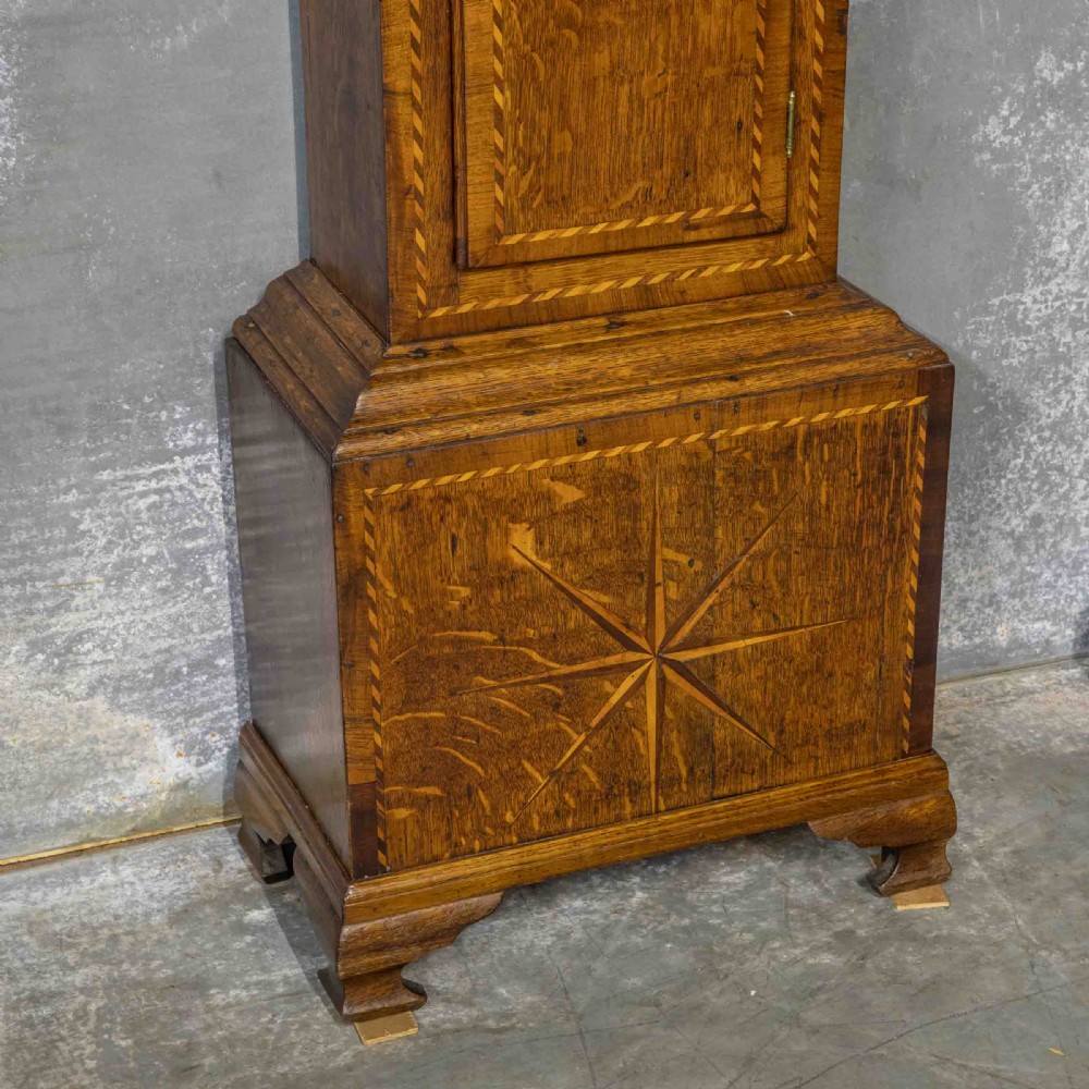 A tall Georgian carved oak longcase clock featuring an arched fretwork pediment, a brass square dial with Roman numerals, star inlay detailing on the trunk door, and a plinth base. View VII