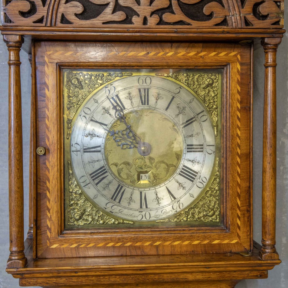 A tall Georgian carved oak longcase clock featuring an arched fretwork pediment, a brass square dial with Roman numerals, star inlay detailing on the trunk door, and a plinth base. View IX