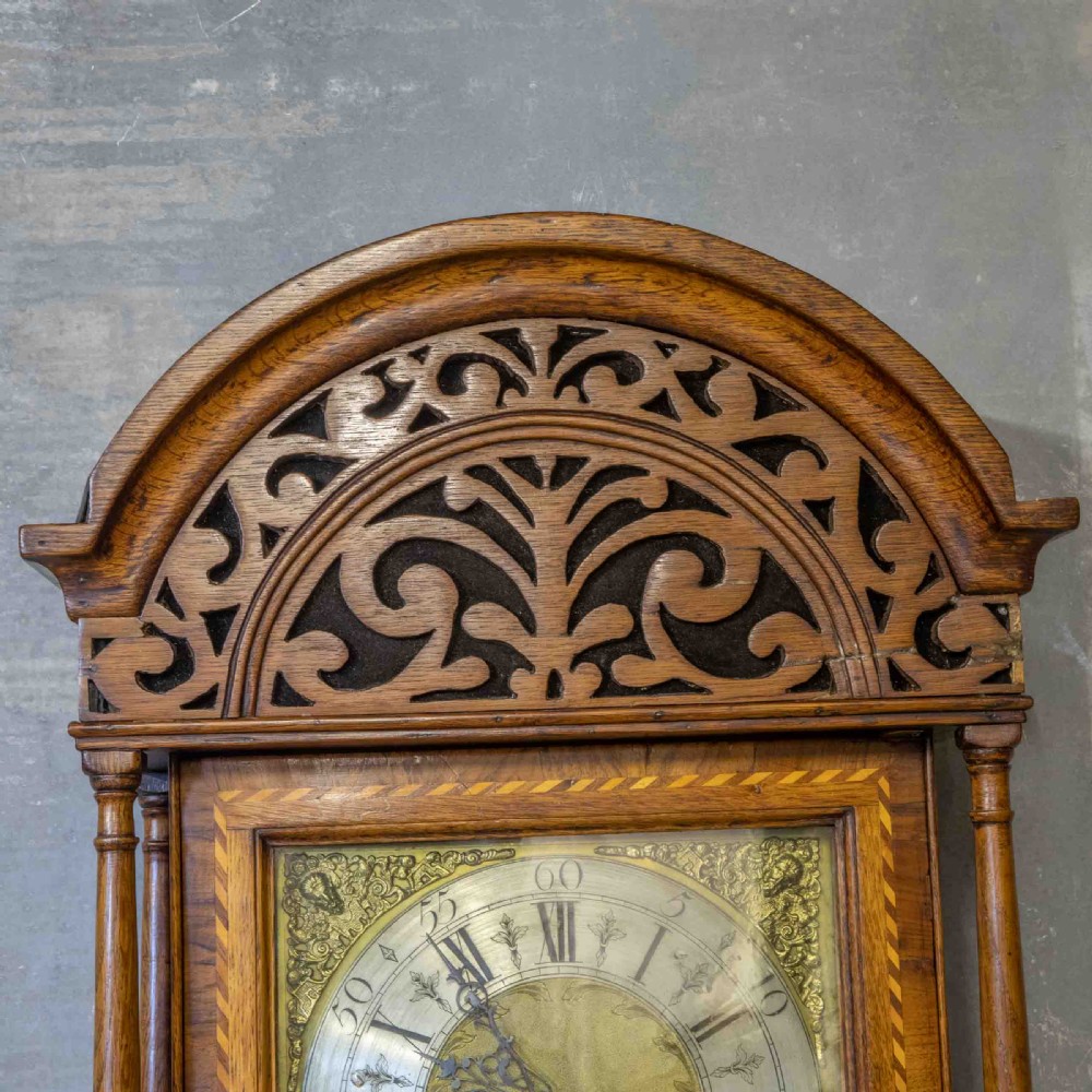 A tall Georgian carved oak longcase clock featuring an arched fretwork pediment, a brass square dial with Roman numerals, star inlay detailing on the trunk door, and a plinth base. View X