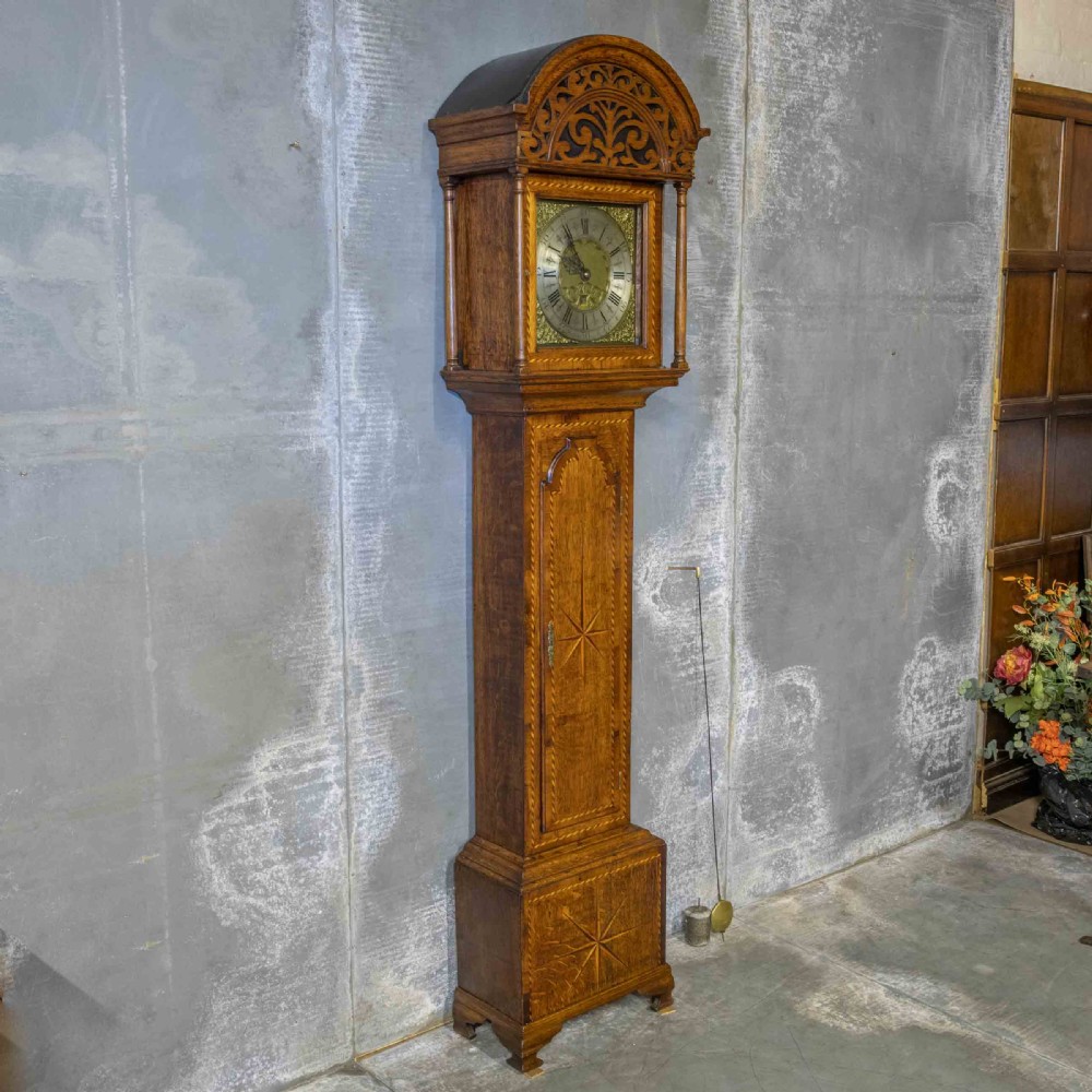 A tall Georgian carved oak longcase clock featuring an arched fretwork pediment, a brass square dial with Roman numerals, star inlay detailing on the trunk door, and a plinth base. View XII