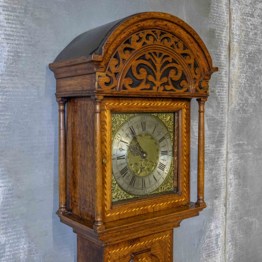 A tall Georgian carved oak longcase clock featuring an arched fretwork pediment, a brass square dial with Roman numerals, star inlay detailing on the trunk door, and a plinth base. View XIII