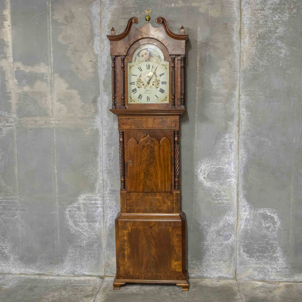 A Georgian mahogany longcase clock featuring a swan-neck pediment with a brass finial, spiral quarter columns, and a hand-painted arch dial.