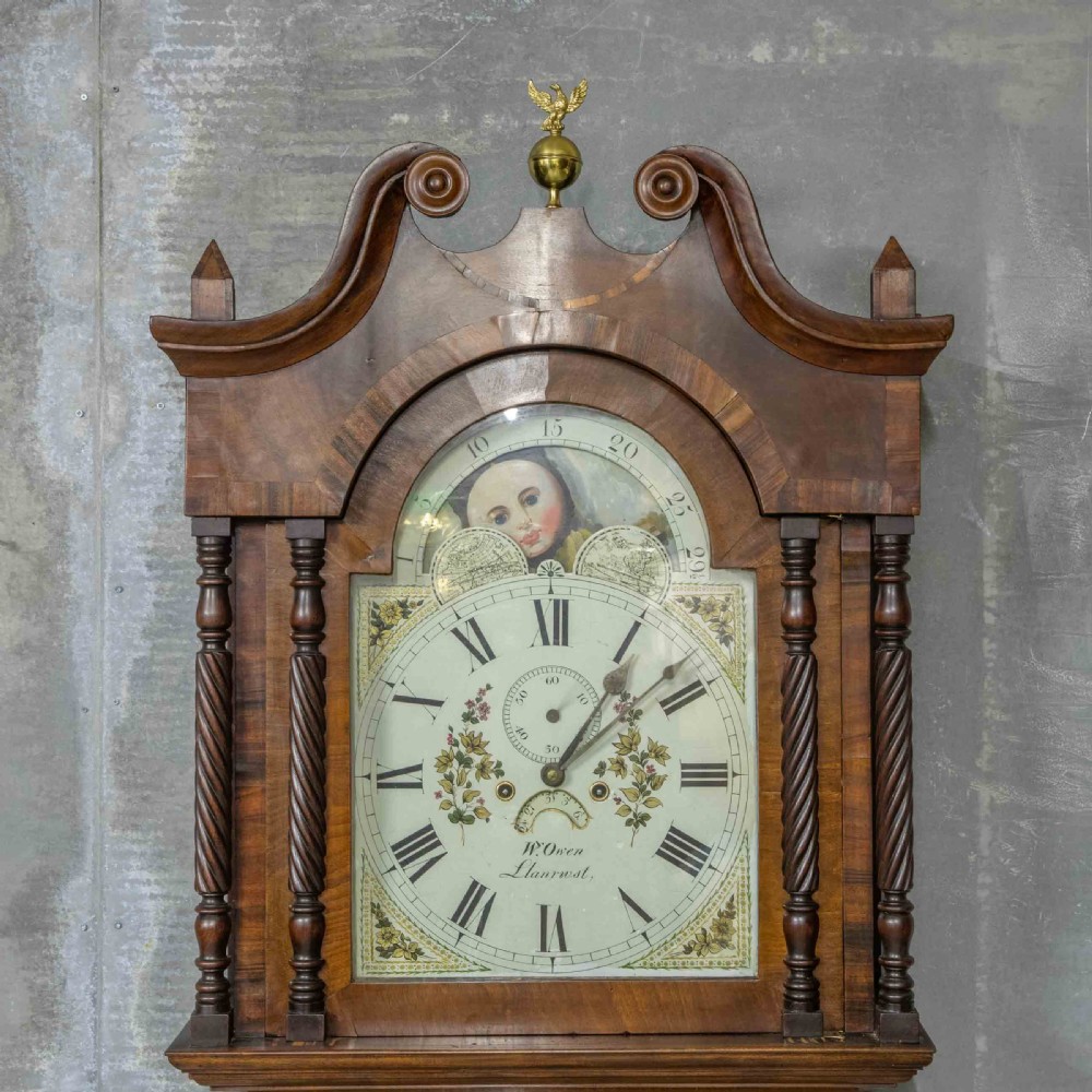 A Georgian mahogany longcase clock featuring a swan-neck pediment with a brass finial, spiral quarter columns, and a hand-painted arch dial. View V