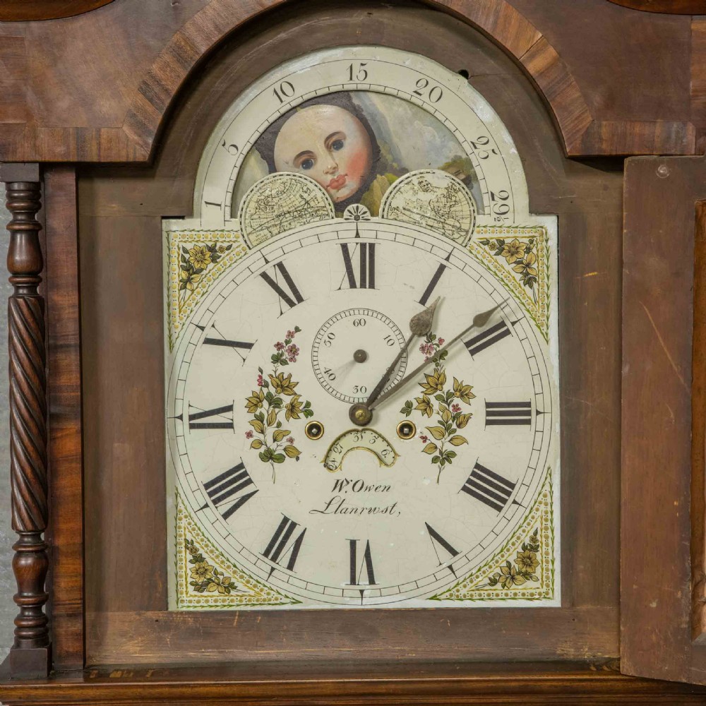 A Georgian mahogany longcase clock featuring a swan-neck pediment with a brass finial, spiral quarter columns, and a hand-painted arch dial. View VII