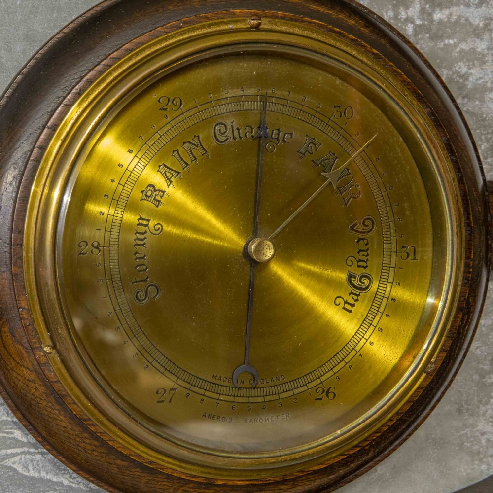 A wall-mounted carved oak coat rack featuring a central round brass aneroid barometer flanked by two double brass hooks. View IV