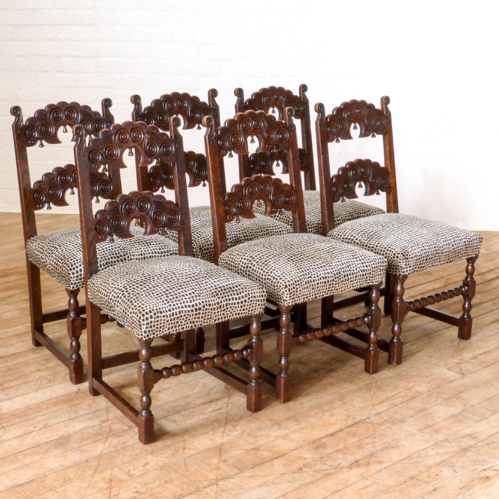 A set of six dark oak Derbyshire style dining chairs featuring intricately carved crescent backs, bobbin-turned front stretchers, and patterned upholstered seats.