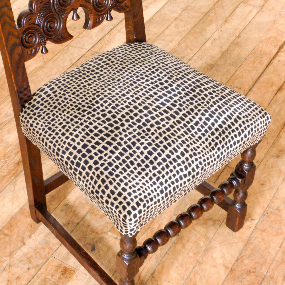 A set of six dark oak Derbyshire style dining chairs featuring intricately carved crescent backs, bobbin-turned front stretchers, and patterned upholstered seats. View VII