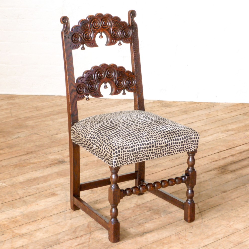 A set of six dark oak Derbyshire style dining chairs featuring intricately carved crescent backs, bobbin-turned front stretchers, and patterned upholstered seats. View IX