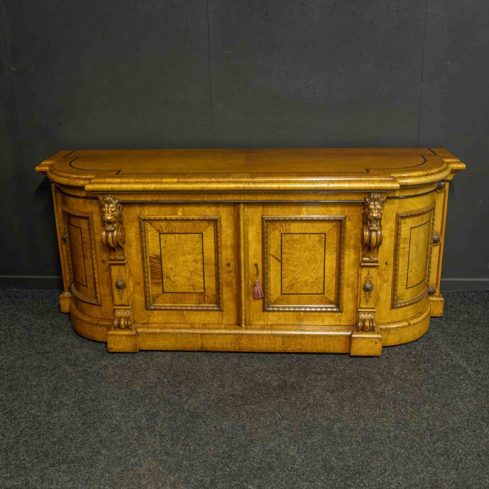A Victorian pollard oak credenza featuring curved breakfront ends, ebonised geometric line inlay, and carved lion mask corbels.