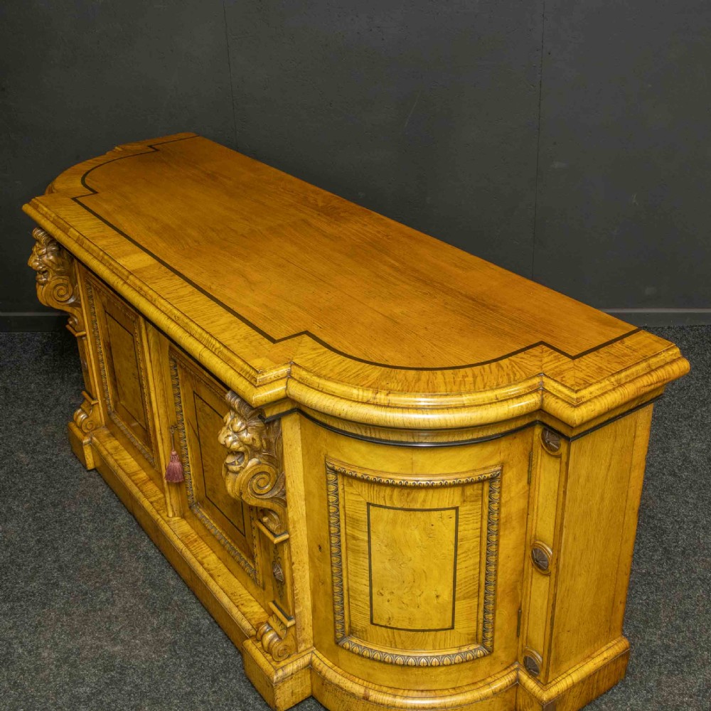 A Victorian pollard oak credenza featuring curved breakfront ends, ebonised geometric line inlay, and carved lion mask corbels. View X
