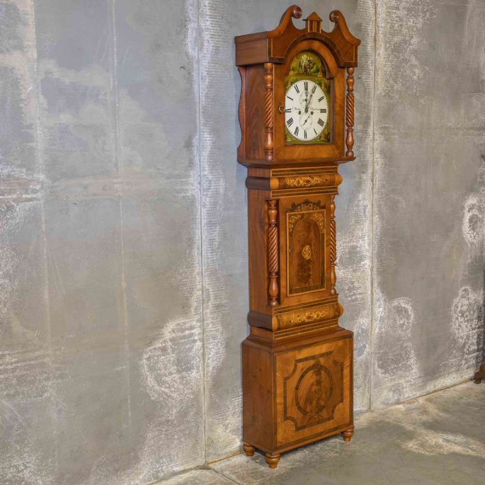 A tall Georgian mahogany longcase clock featuring a swan-neck pediment, turned side columns, floral marquetry inlays, and a painted clock face with Roman numerals.