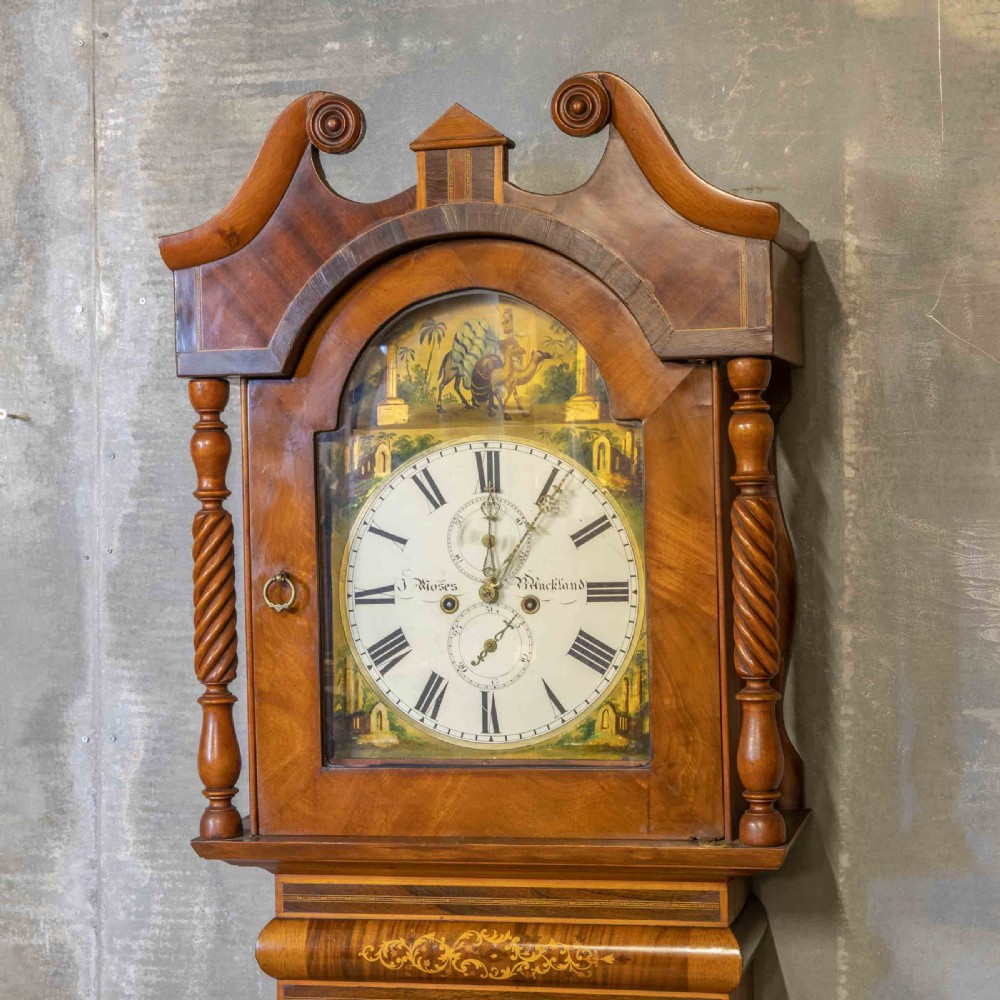 A tall Georgian mahogany longcase clock featuring a swan-neck pediment, turned side columns, floral marquetry inlays, and a painted clock face with Roman numerals. View IV