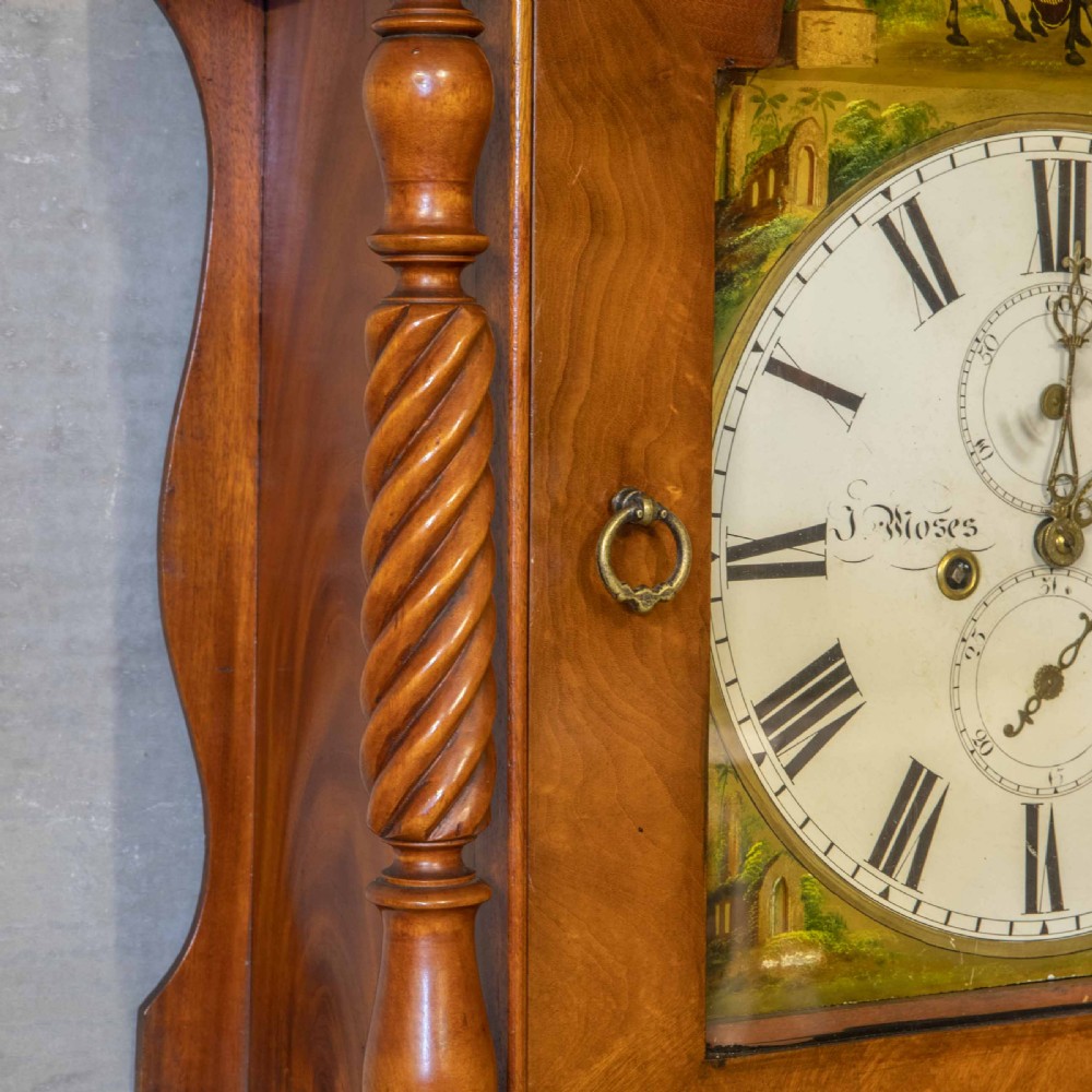 A tall Georgian mahogany longcase clock featuring a swan-neck pediment, turned side columns, floral marquetry inlays, and a painted clock face with Roman numerals. View VI