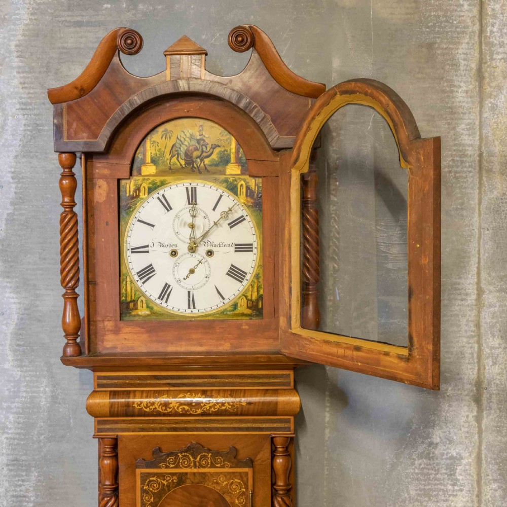 A tall Georgian mahogany longcase clock featuring a swan-neck pediment, turned side columns, floral marquetry inlays, and a painted clock face with Roman numerals. View VII