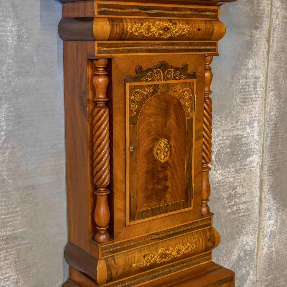 A tall Georgian mahogany longcase clock featuring a swan-neck pediment, turned side columns, floral marquetry inlays, and a painted clock face with Roman numerals. View X
