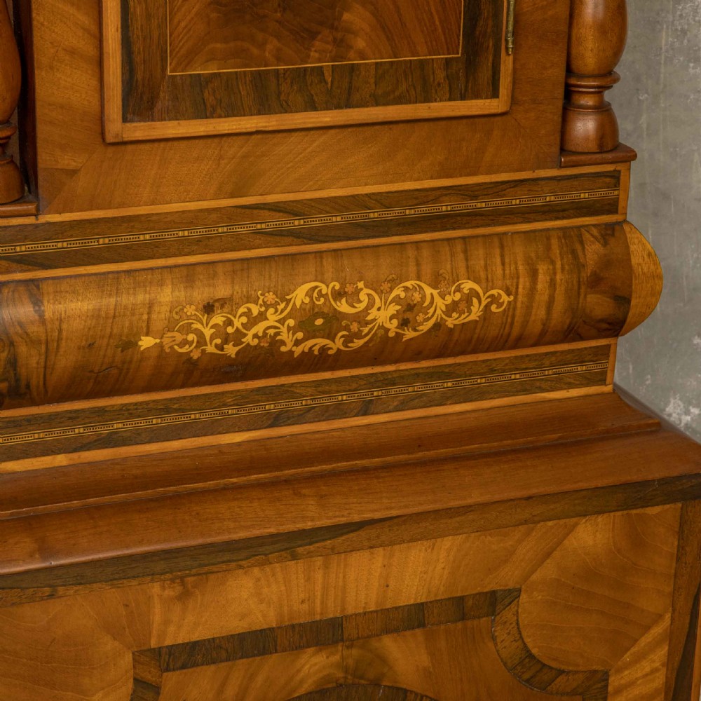 A tall Georgian mahogany longcase clock featuring a swan-neck pediment, turned side columns, floral marquetry inlays, and a painted clock face with Roman numerals. View XII
