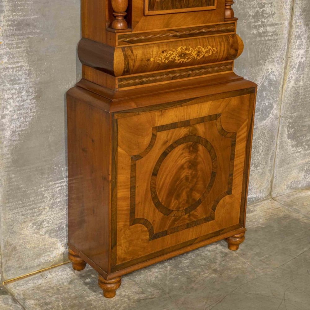 A tall Georgian mahogany longcase clock featuring a swan-neck pediment, turned side columns, floral marquetry inlays, and a painted clock face with Roman numerals. View XIV