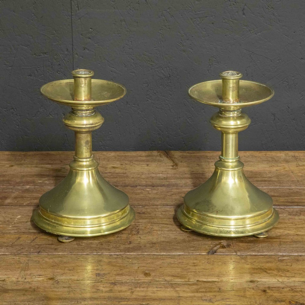A pair of Victorian solid brass pricket candlesticks featuring wide circular drip pans, turned knopped stems, and broad bell-shaped bases.