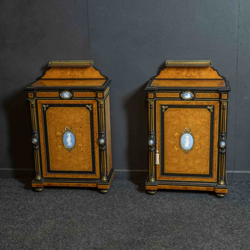 A pair of Victorian ebonised and amboyna pier cabinets featuring raised brass galleries and central blue porcelain Jasperware plaques.