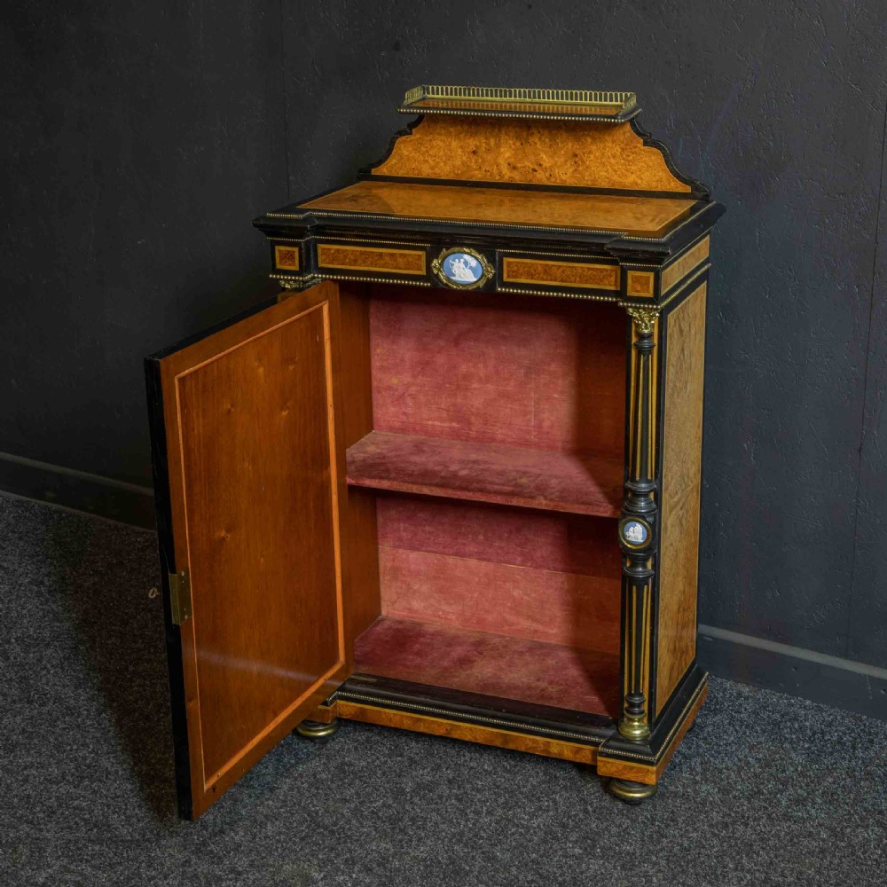 A pair of Victorian ebonised and amboyna pier cabinets featuring raised brass galleries and central blue porcelain Jasperware plaques. View VI