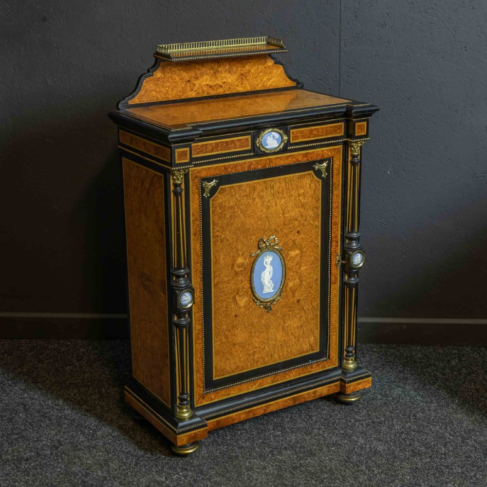 A pair of Victorian ebonised and amboyna pier cabinets featuring raised brass galleries and central blue porcelain Jasperware plaques. View X