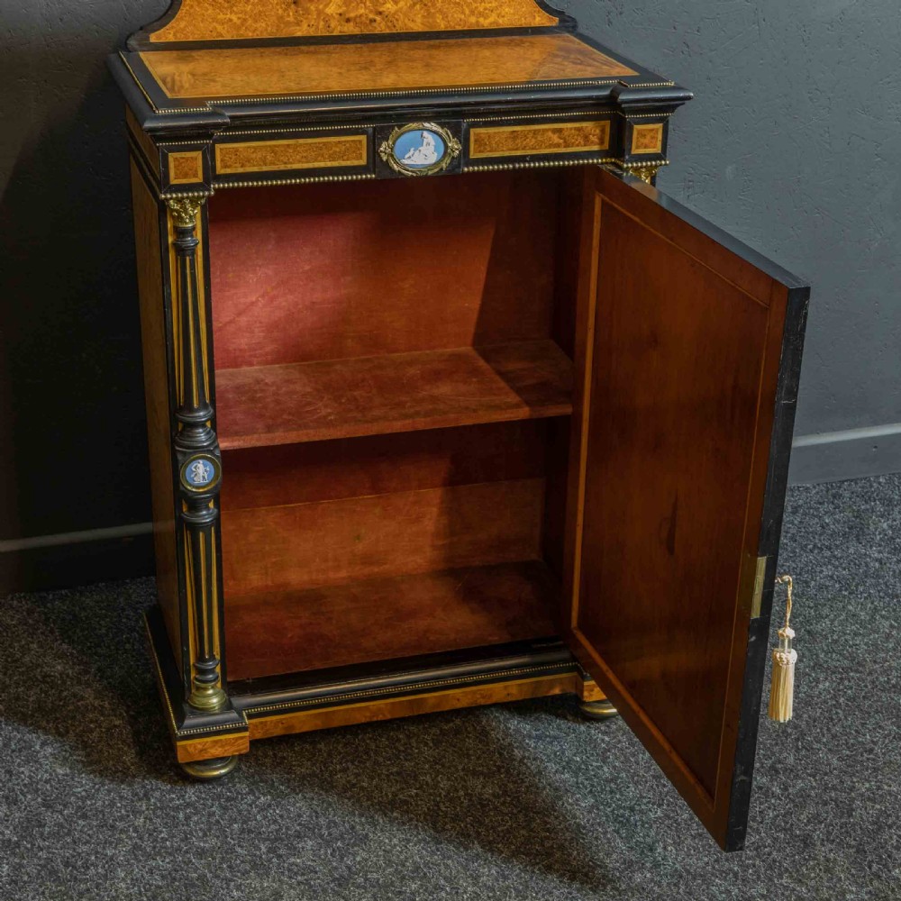A pair of Victorian ebonised and amboyna pier cabinets featuring raised brass galleries and central blue porcelain Jasperware plaques. View XIX