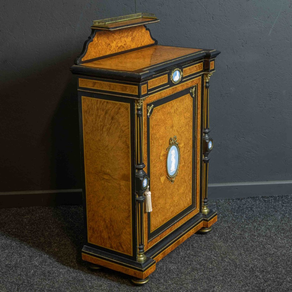 A pair of Victorian ebonised and amboyna pier cabinets featuring raised brass galleries and central blue porcelain Jasperware plaques. View XXI