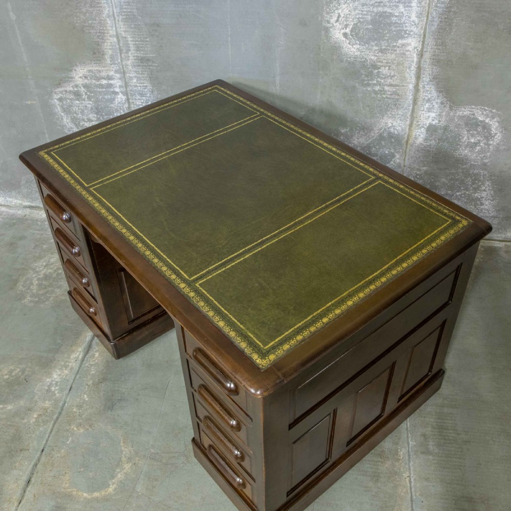 An Edwardian walnut pedestal desk featuring a green gold-tooled leather writing surface, nine drawers with integrated wooden handles, and a plinth base. View III