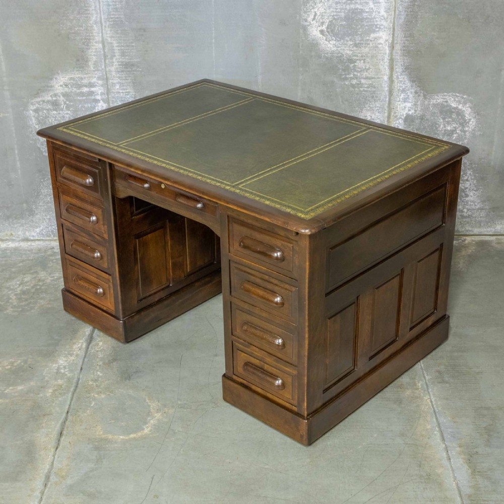 An Edwardian walnut pedestal desk featuring a green gold-tooled leather writing surface, nine drawers with integrated wooden handles, and a plinth base. View VI