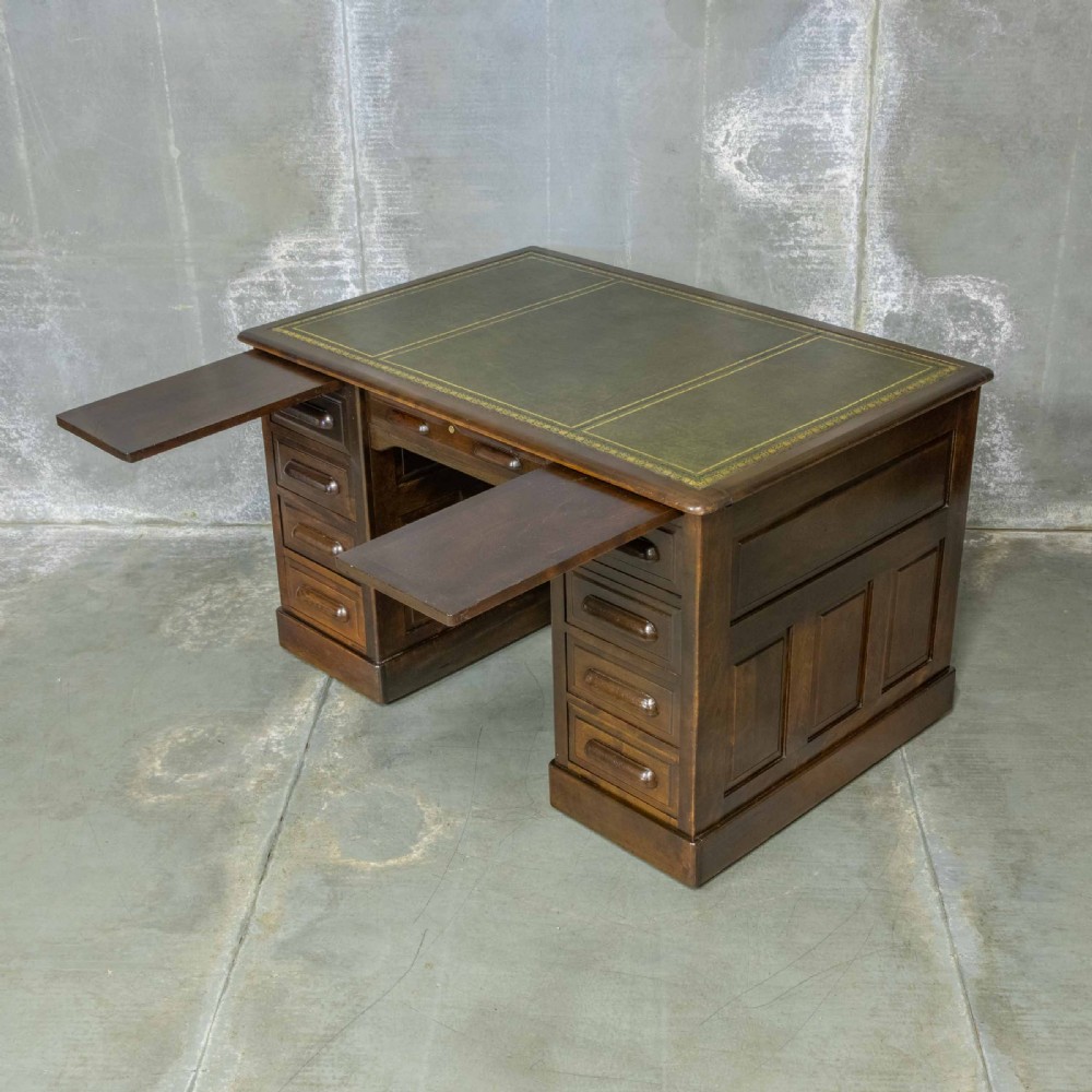 An Edwardian walnut pedestal desk featuring a green gold-tooled leather writing surface, nine drawers with integrated wooden handles, and a plinth base. View VII