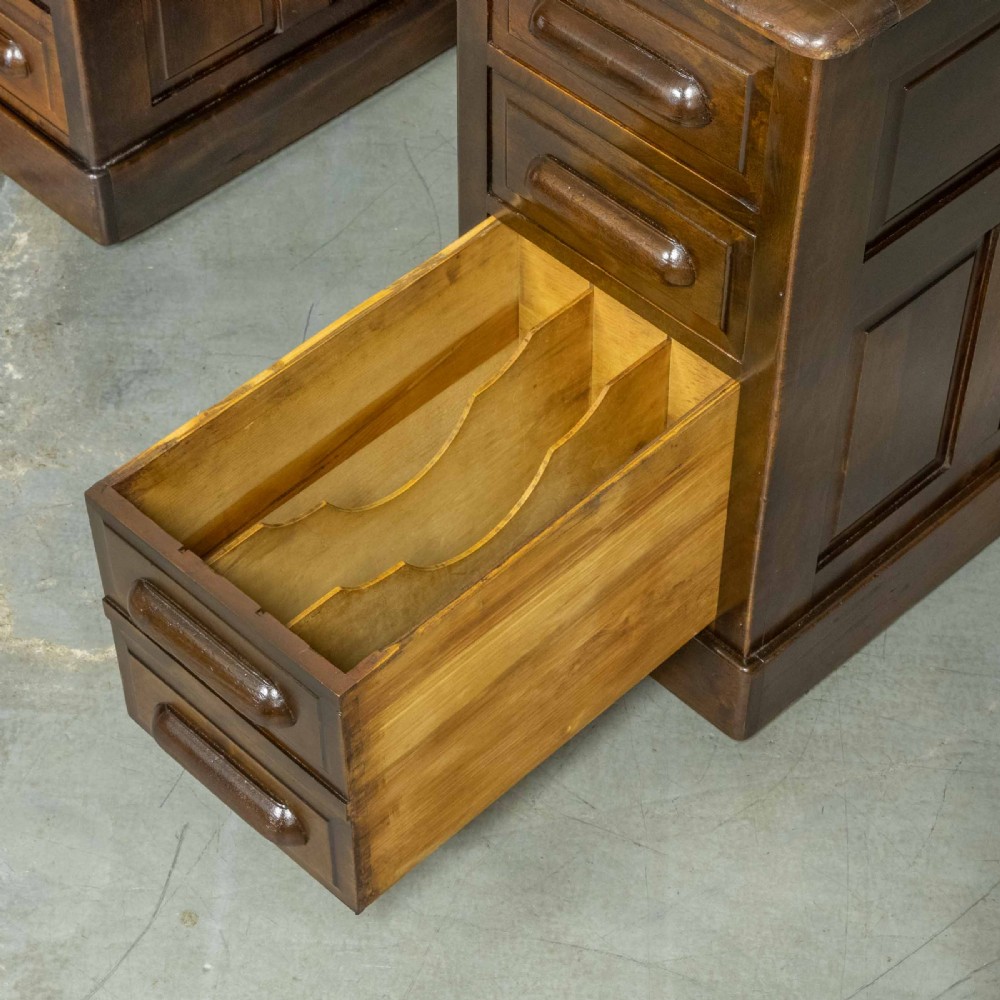 An Edwardian walnut pedestal desk featuring a green gold-tooled leather writing surface, nine drawers with integrated wooden handles, and a plinth base. View VIII