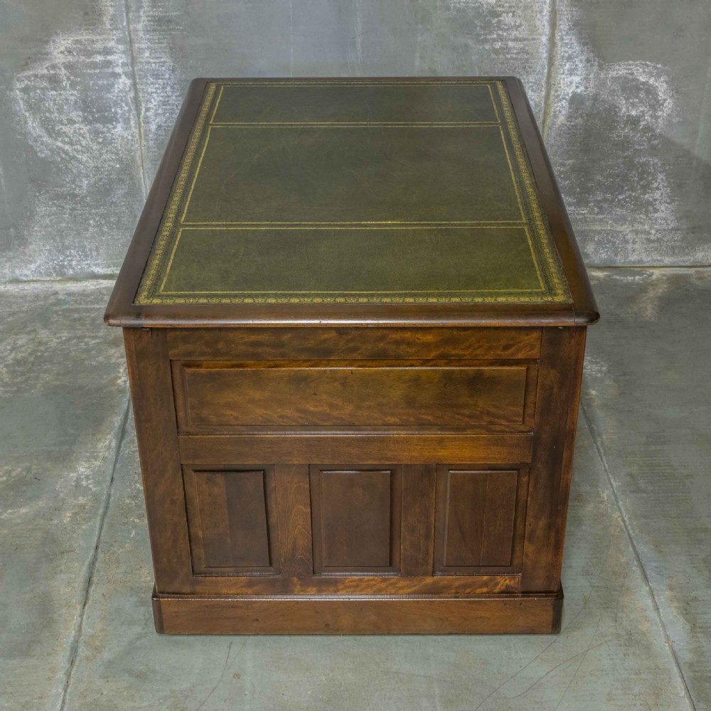 An Edwardian walnut pedestal desk featuring a green gold-tooled leather writing surface, nine drawers with integrated wooden handles, and a plinth base. View X