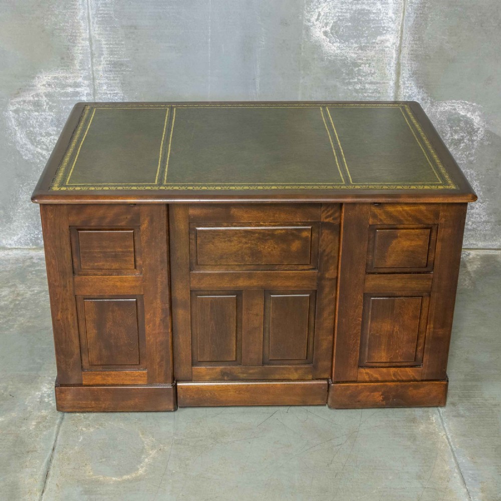 An Edwardian walnut pedestal desk featuring a green gold-tooled leather writing surface, nine drawers with integrated wooden handles, and a plinth base. View XI
