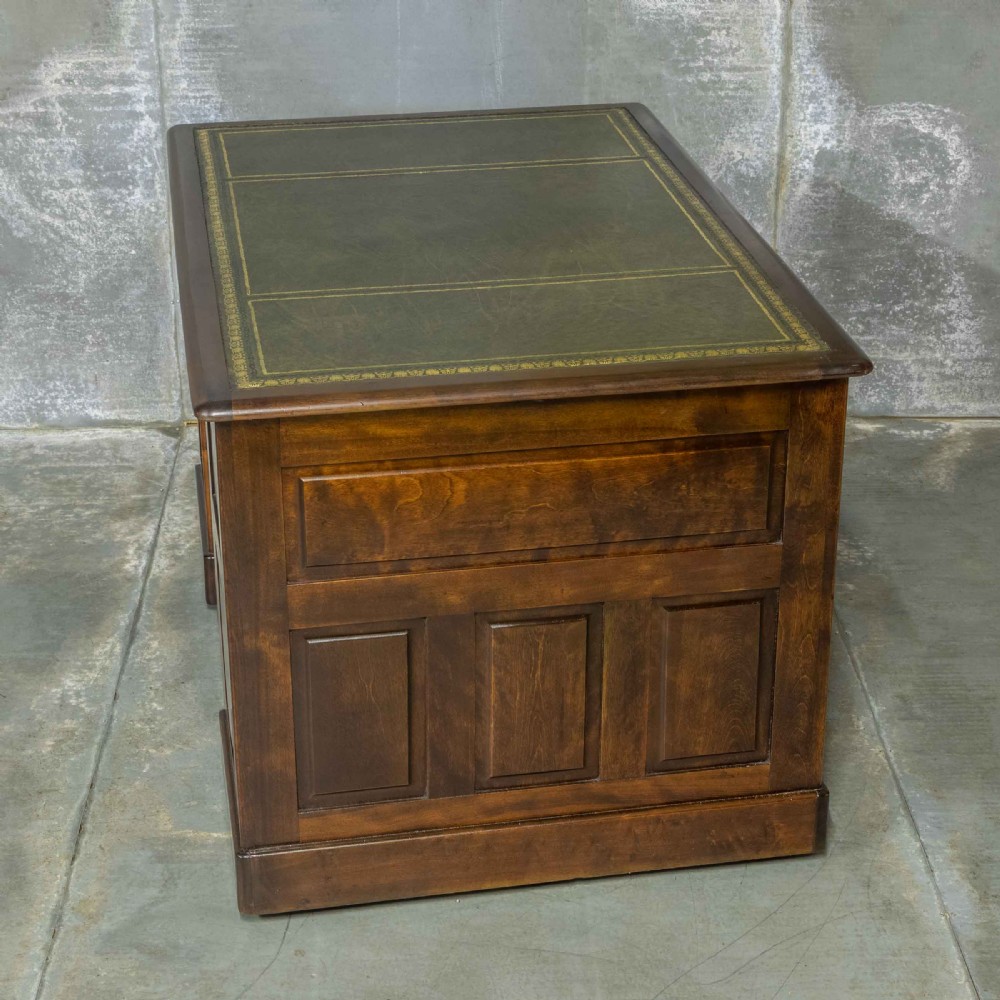 An Edwardian walnut pedestal desk featuring a green gold-tooled leather writing surface, nine drawers with integrated wooden handles, and a plinth base. View XII
