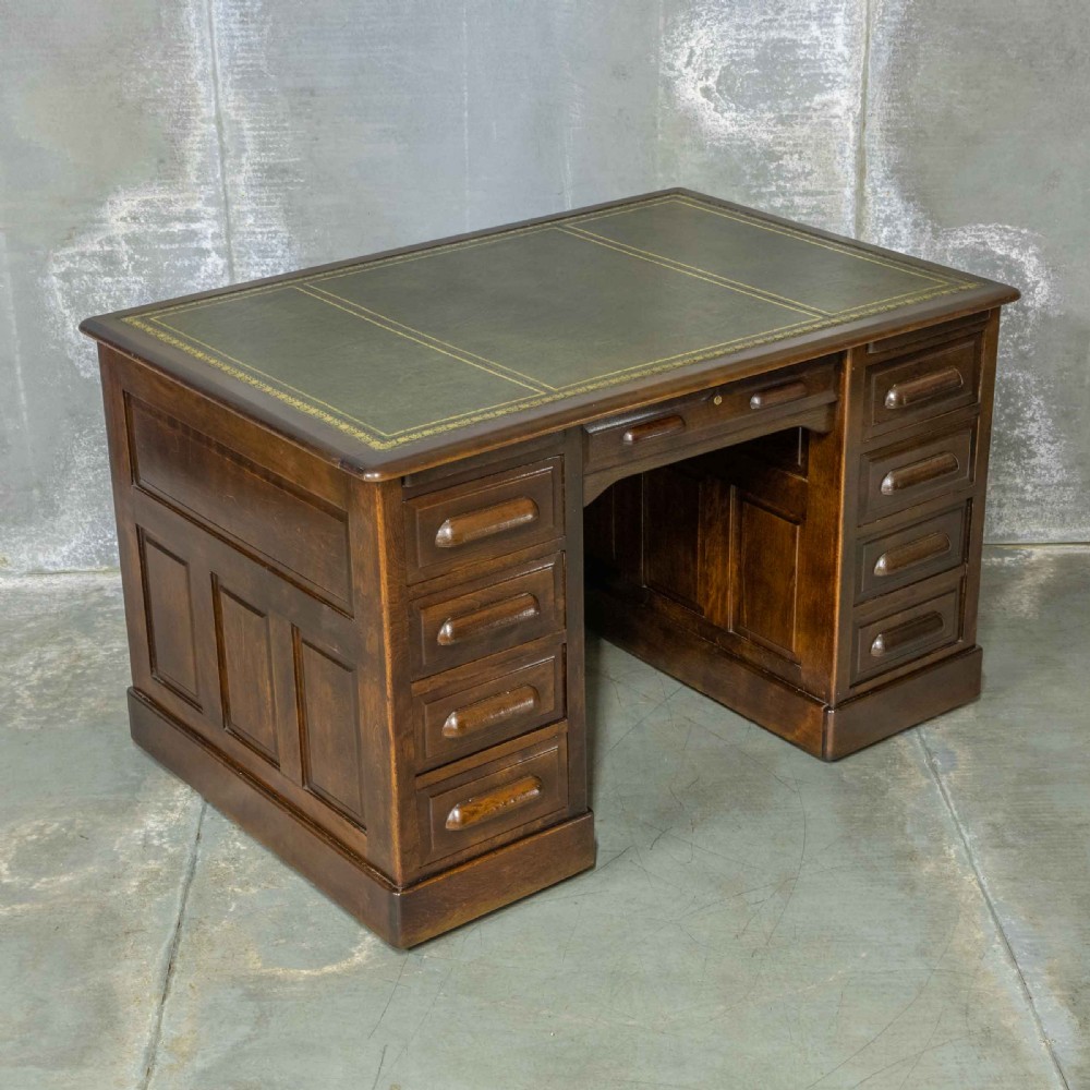 An Edwardian walnut pedestal desk featuring a green gold-tooled leather writing surface, nine drawers with integrated wooden handles, and a plinth base. View XIII