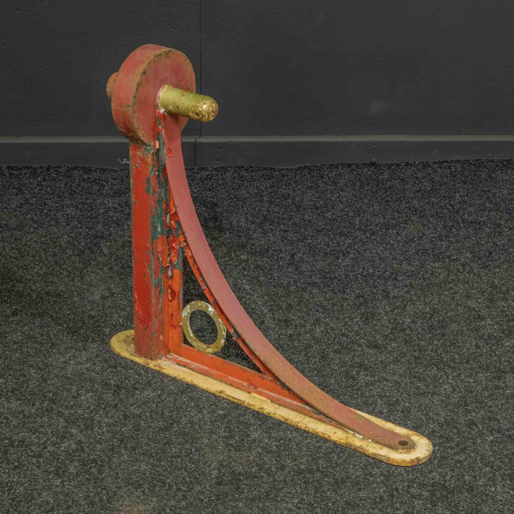 A heavy red painted cast iron wall bracket with a curved support bar and circular motif, showing distressed paint and metal details.