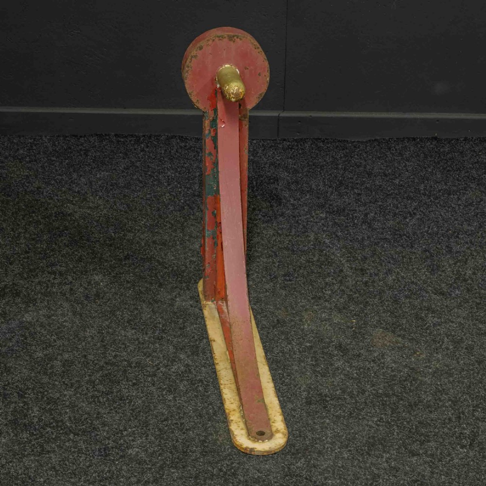 A heavy red painted cast iron wall bracket with a curved support bar and circular motif, showing distressed paint and metal details. View II
