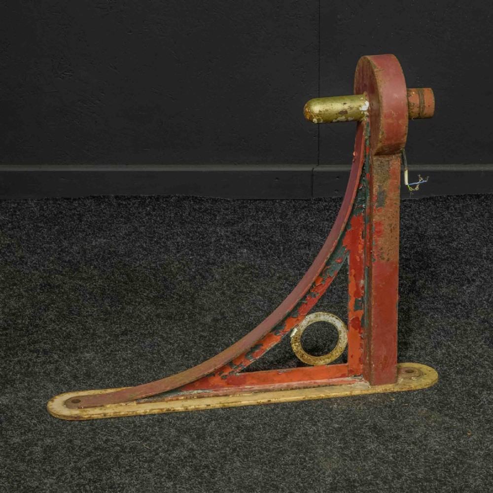 A heavy red painted cast iron wall bracket with a curved support bar and circular motif, showing distressed paint and metal details. View III