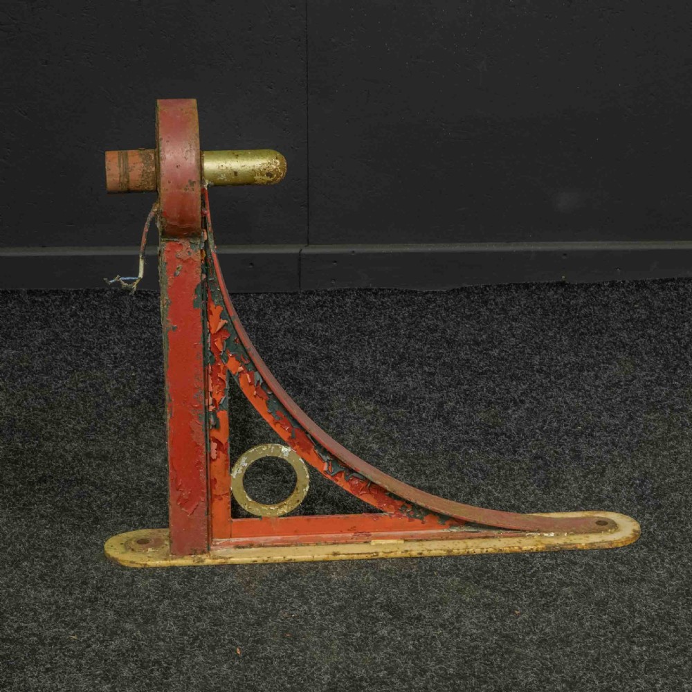 A heavy red painted cast iron wall bracket with a curved support bar and circular motif, showing distressed paint and metal details. View V