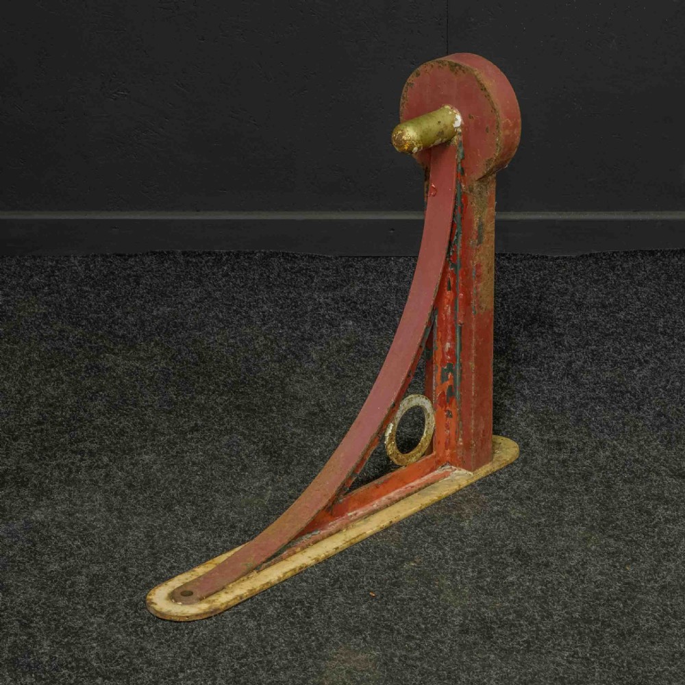 A heavy red painted cast iron wall bracket with a curved support bar and circular motif, showing distressed paint and metal details. View VI