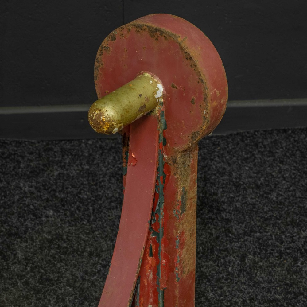 A heavy red painted cast iron wall bracket with a curved support bar and circular motif, showing distressed paint and metal details. View VII