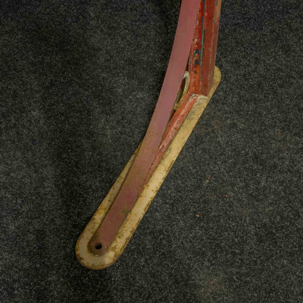 A heavy red painted cast iron wall bracket with a curved support bar and circular motif, showing distressed paint and metal details. View VIII